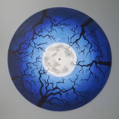 a blue plate with black branches and a full moon in the sky on it's side