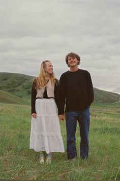 a man and woman standing in a field holding hands