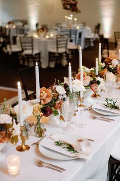 the table is set with white and gold plates, silverware, candles, and flowers