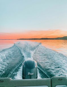 the back end of a boat traveling on water at sunset or sunrise with clouds in the sky