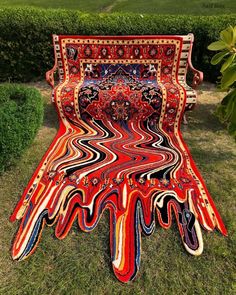 an artisticly designed bench sitting in the middle of a grassy area with bushes behind it