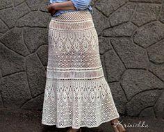 a woman standing in front of a stone wall wearing a white crochet skirt