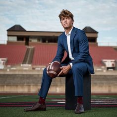 a man in a suit and tie sitting on top of a football field holding a ball