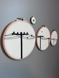 three embroidered wall hangings with birds sitting on telephone wires in front of grey background