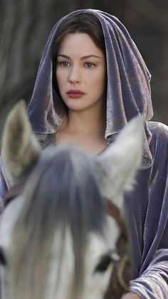 a woman in a robe riding on the back of a white horse with a gray blanket over her head