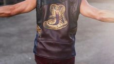 a man wearing a leather vest with a snake on it's back and his arms stretched out