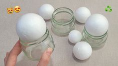 a hand is holding an egg in front of several glass jars with white eggs inside