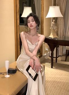 a woman in a white dress is sitting on a table and holding a black purse