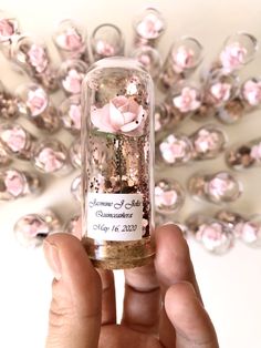 a hand holding a tiny bottle filled with pink flowers