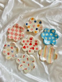 six flower shaped dishes sitting on top of a white cloth covered tablecloth, all decorated in different colors and designs