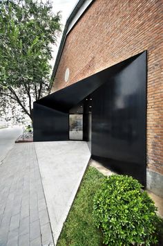 an open door on the side of a brick building with grass and trees around it