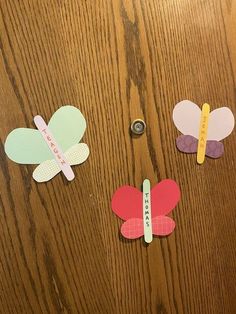 three pieces of paper cut out to look like butterflies on a wooden surface with measuring tape