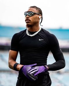 a man in black shirt and purple gloves holding his hand on his hip while wearing sunglasses