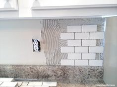 a kitchen counter with white and gray tiles on the backsplash, an electrical outlet in the middle