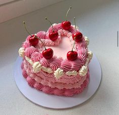 a heart shaped pink cake with cherries on top is sitting on a white plate