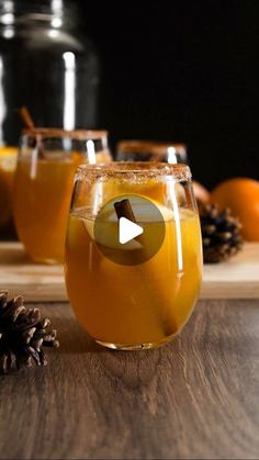 several glasses filled with liquid sitting on top of a wooden table next to pine cones