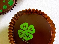 two cupcakes decorated with shamrock leaves and the hh logo on each one