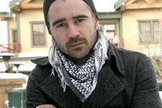 a man wearing a hat and scarf standing in front of a house with snow on the ground