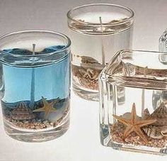 three clear glass vases filled with sand and starfish on top of a white surface