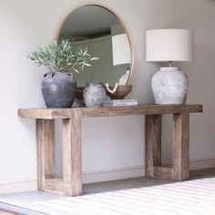 a table with two vases and a mirror on top of it next to a lamp