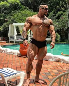 a man standing in front of a swimming pool wearing a black swim suit and sunglasses