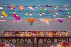 a long table is set up on the beach for a party with colorful flags and candles