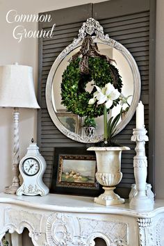 a white fireplace mantle with a mirror and flowers on it, next to a lamp