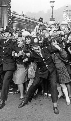 a group of people standing around each other in front of a fence with police officers