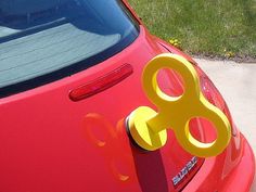 a red car parked on the side of a road with a pair of yellow scissors attached to it