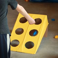 a person standing next to a yellow box with holes in it and one hand reaching for something