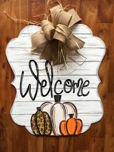 a welcome sign hanging on the side of a wooden wall with pumpkins and burlocks