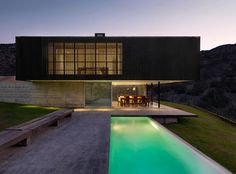 a house with a pool in front of it at night, surrounded by grass and mountains