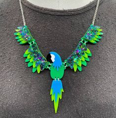 Polly Parrot 🦜 necklace is a fun quirky piece. It's a statement piece that will look great with any outfit.  The necklace is delicately made with green, blue and our fabulous glitter green acrylic. The wings are linked together using jump rings and connected to a curb chain.  If you have any questions drop us a line!💌 We are more than happy to help! 😁 To clean your necklace you can simply wipe with a glasses cloth or soft cloth to remove finger marks. Acrylic is a fragile material so please store in a jewellery box to prevent damage.  As ever for safety please keep away from children. Trendy Resin Necklaces For Party, Fun Resin Jewelry For Parties, Fun Resin Jewelry For Party, Fun Resin Party Jewelry, Unique Green Resin Necklaces, Unique Green Resin Necklace, Quirky Handmade Green Jewelry, Green Novelty Resin Jewelry, Handmade Green Novelty Necklace