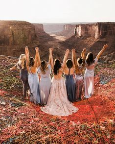 a group of women standing next to each other on top of a cliff with their arms in the air