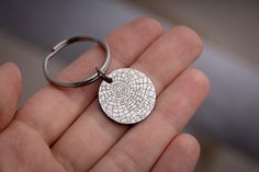 a hand holding a metal keychain with a circular design on it's side