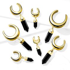 six pairs of black and gold earrings on a white surface with one pair hanging off the side