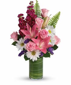 a vase filled with pink and white flowers on top of a green planter next to ferns