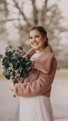 a woman in a white dress holding a bouquet of flowers and smiling at the camera