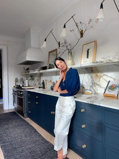 a woman standing in a kitchen next to blue cabinets and counter tops with lights above her