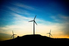 three windmills on top of a hill at sunset