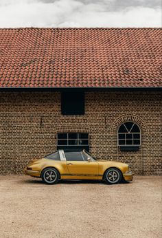 a yellow sports car parked in front of a brick building with a red tiled roof