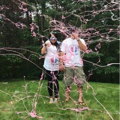 two people standing next to each other in the grass with pink streamers all over them