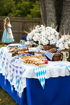 a table topped with lots of food next to a forest filled with white and blue flowers