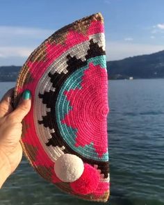 a person holding up a colorful piece of crocheted material on the water's edge