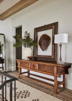 a wooden table with a mirror and vase on top of it next to a stair case