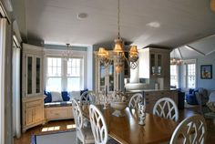 a chandelier hanging from the ceiling in a dining room with white chairs and wooden table