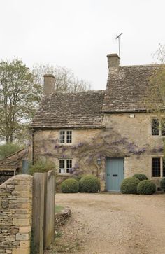 an old stone house with a blue door and some bushes in front of the building