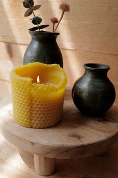 two vases with flowers in them on a table next to a candle and some wax