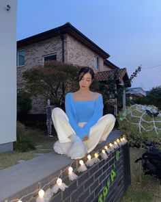 a woman sitting on top of a brick wall next to a tree with lights in front of her