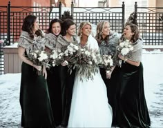 a group of women standing next to each other in front of a fence with snow on the ground